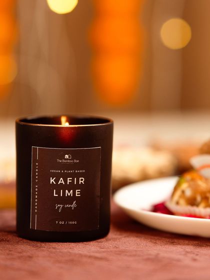A close-up of a "Kafir Lime" scented candle. The soft focus and warm, blurry background lights create a cozy and intimate mood.