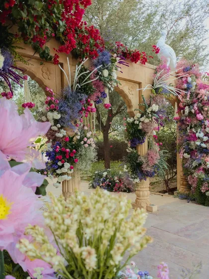 A stunning floral archway in shades of purple and pink, with a white peacock perched atop, creating a fairytale entrance for the wedding ceremony.