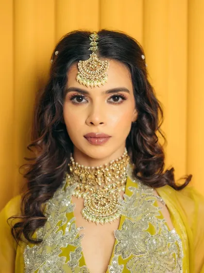 A straight-on portrait showcasing the symmetry and balance of the makeup. The defined brows, soft eyes, and neutral lips work in harmony with the statement jewelry.