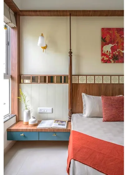 A close-up of the bedside area, featuring a floating drawer in a contrasting blue, a traditional wall sconce, and vibrant artwork.