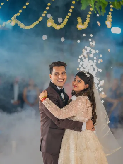 A joyful moment during the first dance, with the groom smiling at the camera, surrounded by sparklers and smoke at their Catholic wedding reception.