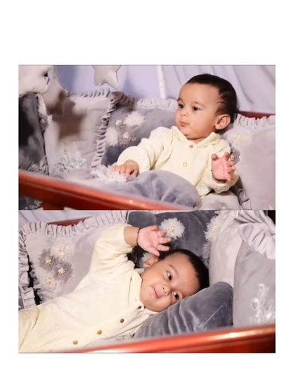 A happy baby enjoying his new cozy corner. He is sitting up and looking content in his crib, which is filled with my soft, custom-made grey velour pillows with floral details.
