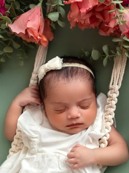 A beautiful floral swing setup against a soft green background. The contrast of the pink flowers and the baby's white outfit is just lovely.