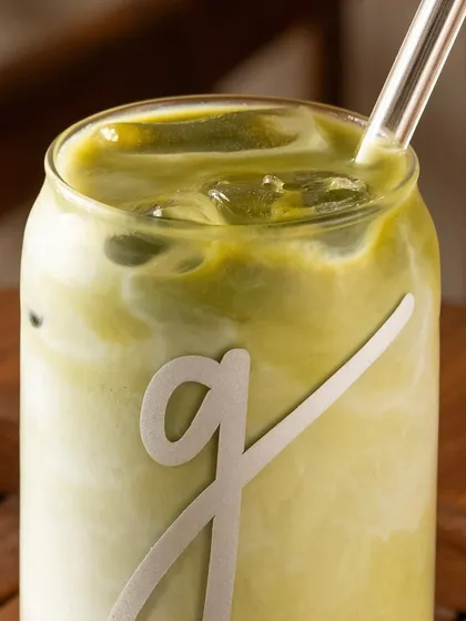 A close-up of the iced matcha latte, showing the texture and the brand's logo on the glass.