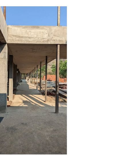A view down the long corridor of one of the homes in the Alibaug commune during construction. The repeating columns create a strong rhythm, framing the natural landscape at the end.