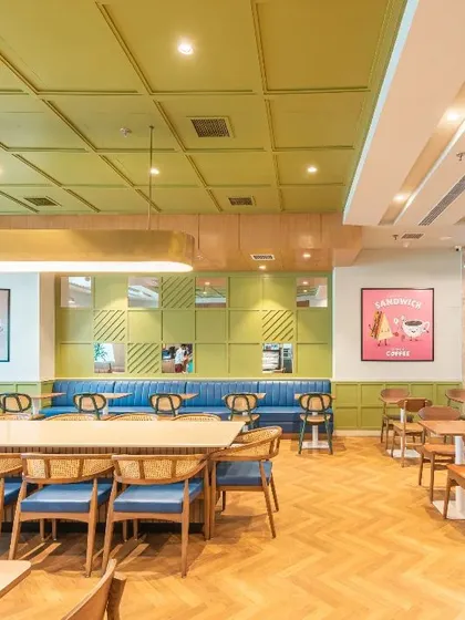 Another view of the hospital cafeteria, showing the use of herringbone wood floors and a green coffered ceiling. These design choices create a space that feels more like a vibrant cafe than a hospital amenity.