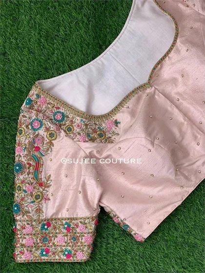 A lovely light pink blouse featuring colorful peacock and floral embroidery. This piece uses a vibrant palette of pink, green, and blue threadwork, perfect for a spring or summer wedding.