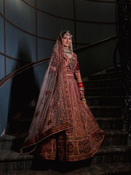 A full-length portrait of the bride on a spiral staircase, her magnificent lehenga cascading down the steps. A picture of pure elegance.