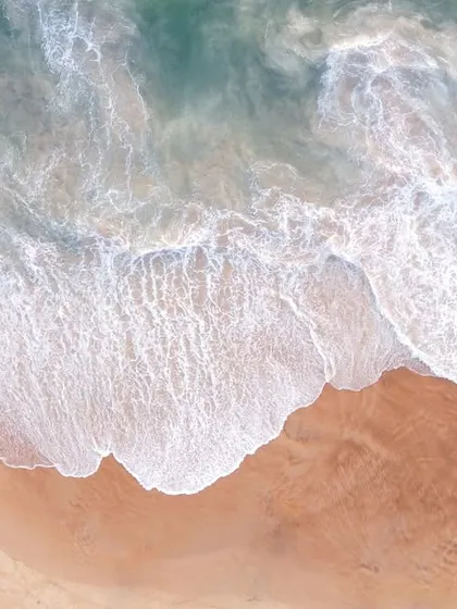 An abstract top-down drone shot capturing the texture of waves washing over a sandy beach, creating a beautiful natural pattern.