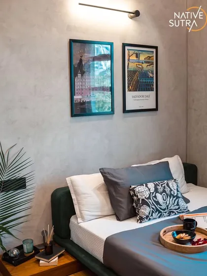 A detail shot showing the careful curation of art and accessories in the loft-style room. The textures of the bedding, the warmth of the wooden side table, and the greenery create a balanced and inviting corner.