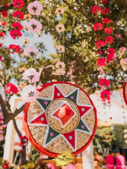 A close-up of a decorative hanging element from the Assamese Haldi. A traditional Jaapi is beautifully embellished and surrounded by hanging paper flowers, celebrating the region's rich craft heritage.