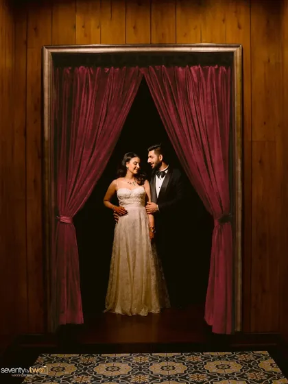 Framed by dramatic red curtains, they look like the stars of their own movie. A theatrical and elegant portrait from their celebration in Siliguri.