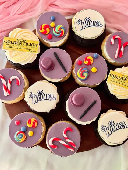 A full set of Willy Wonka inspired cupcakes. The designs feature iconic elements made from fondant like candy canes and lollipops, alongside edible prints of the Wonka logo and a Golden Ticket, all arranged on vanilla and chocolate bases.