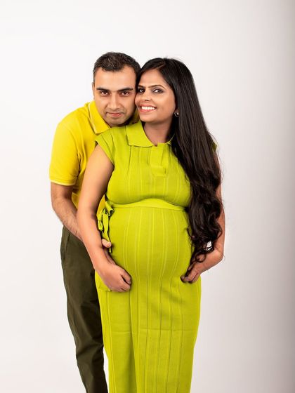 A classic couple's portrait in the studio. The dad-to-be stands behind, embracing the mom-to-be, creating a photo that symbolizes support and partnership.