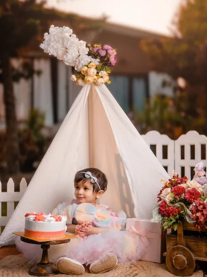 A whimsical garden party to celebrate turning one. This little girl looks like a fairy-tale princess in her rainbow dress, sitting by her cake in a beautiful teepee setup.