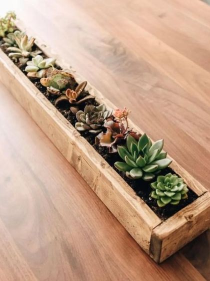 A long, wooden planter box filled with a variety of artificial succulents. This makes a beautiful and modern centerpiece for a long table or a console, offering texture and color without any need for watering.