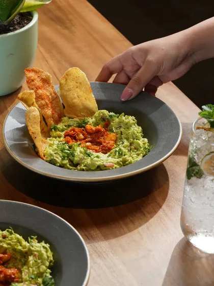 An action shot of guacamole and papad, capturing the moment of enjoyment. The human element makes the image more relatable and the food more desirable.