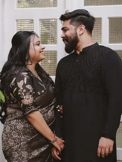 A couple portrait featuring a client in a black Banarasi saree. Her custom blouse is embroidered with delicate floral motifs, adding a touch of elegance to the dark, rich fabric.