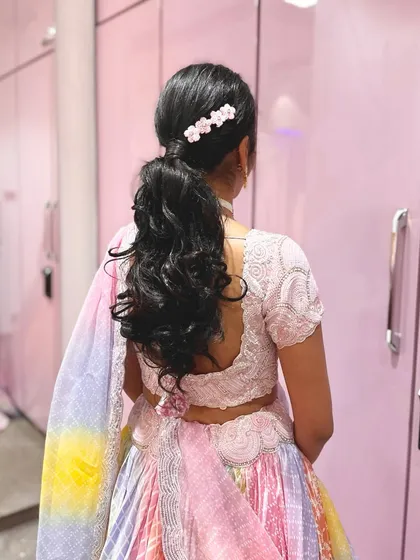 A voluminous ponytail with a small floral clip, created for a bride's Patrika function. This style is both traditional and modern, perfect for a daytime ceremony.