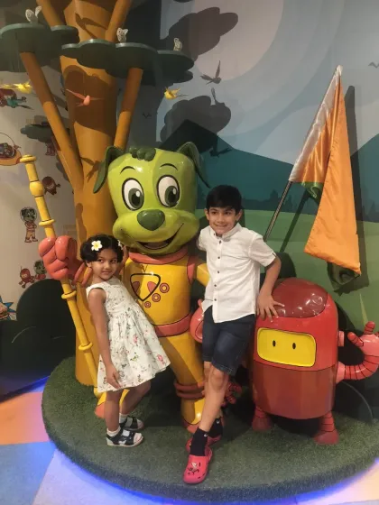 Two siblings smile for a photo with the friendly statues of Tinga Dojo and Boxy.