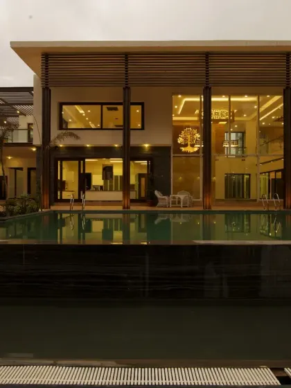 The Sachdeva Farmhouse is designed as a luxurious retreat, organized around a central pool. The double-height glazed façade reflects the glowing interiors at twilight, blurring the lines between the architecture and the surrounding landscape to create a resort-like sanctuary.