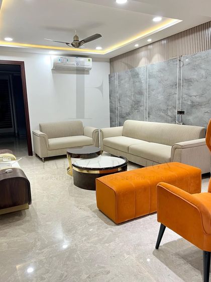 A wider view of the living room, showing the interplay between the neutral sofas and the bold orange accent chairs. The layout is designed to be both social and spacious.