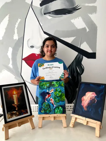 This student's oil paintings are incredible, from the glowing candle to the dynamic koi fish. She's proudly holding her certificate of completion.