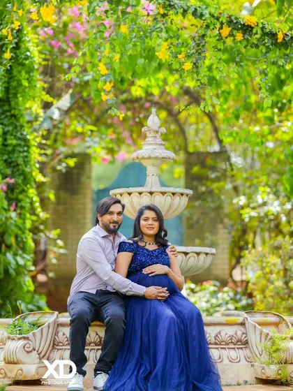 A classic couple's portrait seated by a garden fountain, surrounded by colorful flowers.