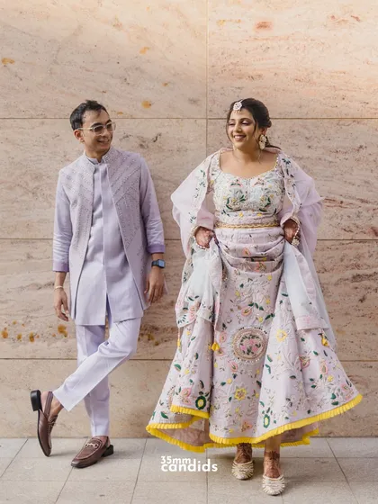 A full-length shot of the couple in their beautiful, coordinated pastel outfits for their Haldi ceremony, showing off the intricate floral embroidery.