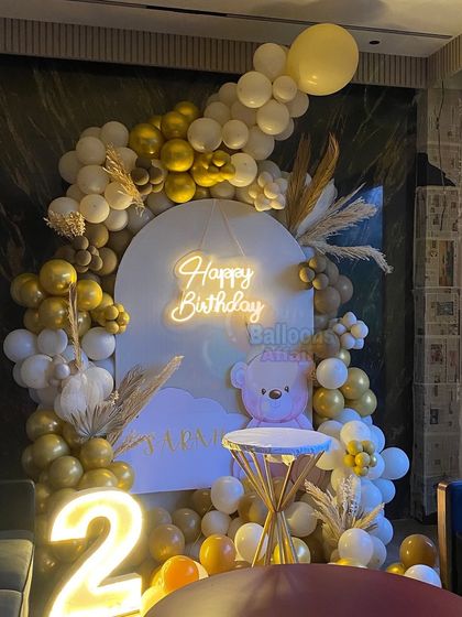 A cozy teddy bear theme for a second birthday. This setup uses a neutral color palette of white, gold, and brown balloons, with a cute bear graphic and a light-up number '2'.
