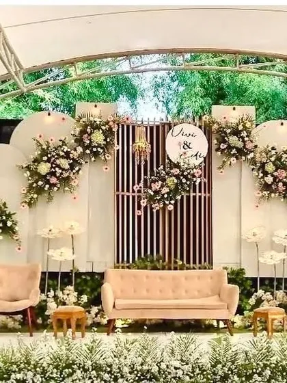 This engagement stage setup is perfect for an outdoor venue. It features modern white arched panels, comfortable lounge seating, and beautiful floral arrangements that complement the natural surroundings.