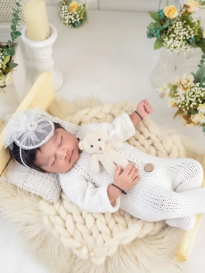 Cuddling a tiny teddy bear, this baby is the picture of serenity. The all-white outfit and floral decor create a classic and angelic newborn portrait.