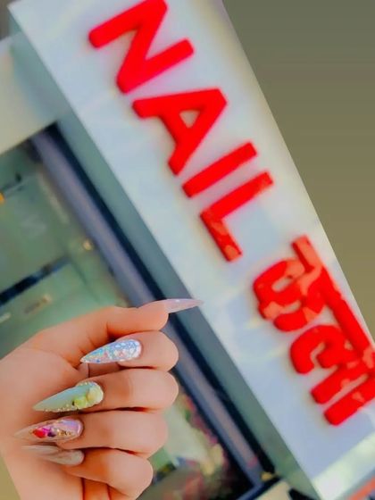 A client holding up her freshly done, artistic nails in front of the Nail Kala studio sign.