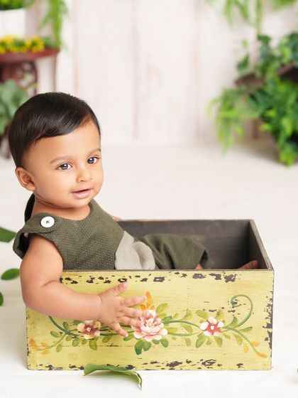 A curious peek from inside a vintage-style box. The natural greenery and his sweet expression make this a charming and timeless portrait.