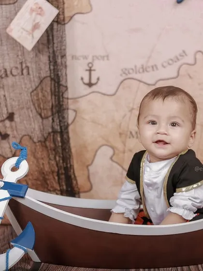 A sweet smile from our little pirate. The setup includes charming details like an anchor, pink flowers, and vintage-style postcards to complete the scene.