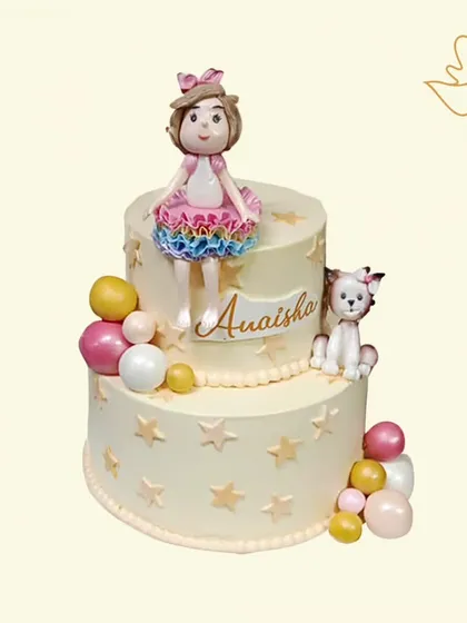 A sweet two-tier cake for a little girl's birthday, featuring a cute doll and her pet cat. The design is adorned with stars and colorful balls for a playful and charming look.