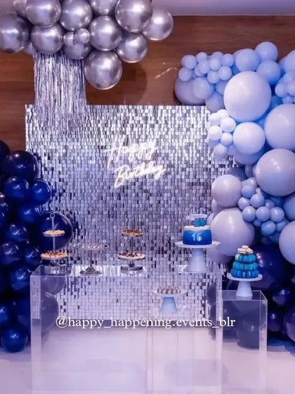A cool and contemporary party theme using shades of navy, light blue, and silver. The clear acrylic dessert table adds a modern touch, allowing the balloon colors and shimmering backdrop to stand out.