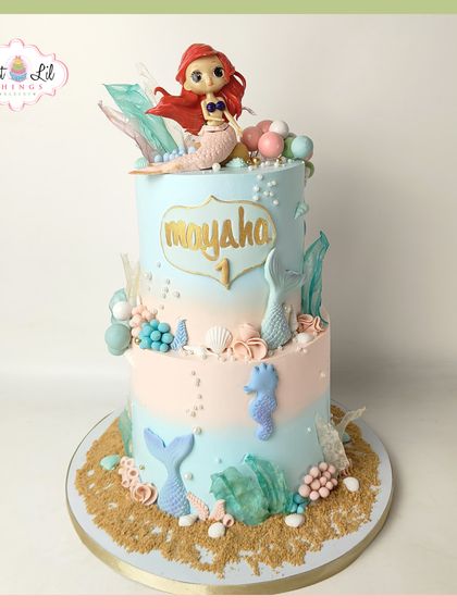 A magical mermaid cake for a first birthday. This two-tiered under-the-sea creation features a sweet Ariel, pastel colors, edible sand, and charming sea creatures like a seahorse.