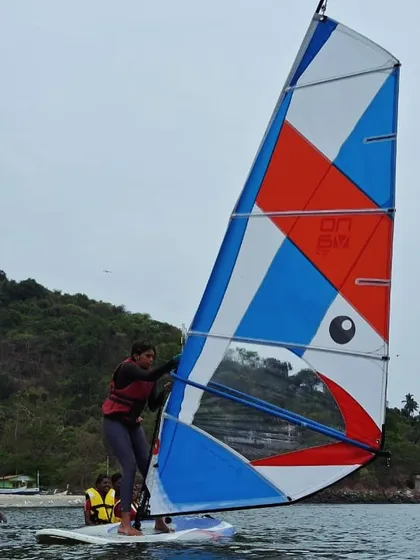 A female participant gets the hang of handling the large sail during her windsurfing lesson in Karwar.
