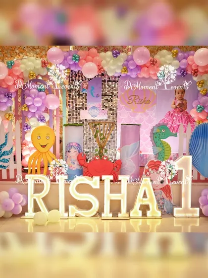 An enchanting 'Under the Sea' first birthday stage for Risha. The decor is filled with mermaid and sea creature cutouts, including an octopus and crab, a sequin backdrop, and pastel balloon arrangements to create a magical underwater world.