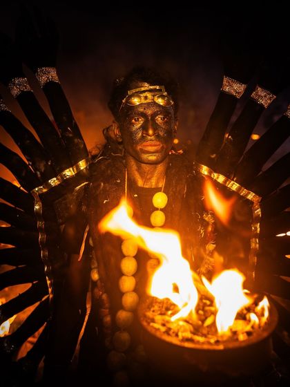A portrait of a devotee with an elaborate costume, holding a fire pot that casts a warm glow on his painted face, highlighting the artistry of the festival.