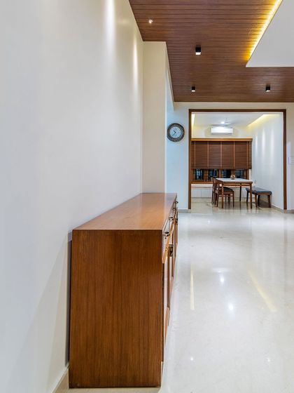 The clean lines of this hallway are created by the contrast between the white walls, the polished marble floor, and the dark wood of the ceiling and furniture.