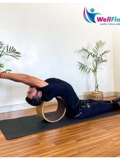 A trainer demonstrates a deep backbend using a yoga wheel. This prop provides support while helping to open up the thoracic spine, which is often tight and can contribute to poor posture and back pain.