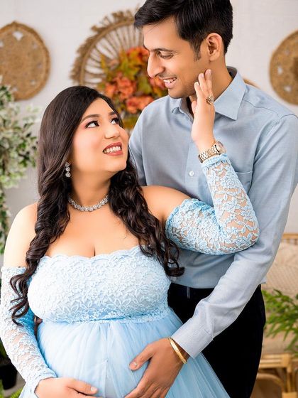 A beautiful moment between the expecting parents, dressed in coordinating shades of blue. The boho studio setting adds a touch of warmth and nature.