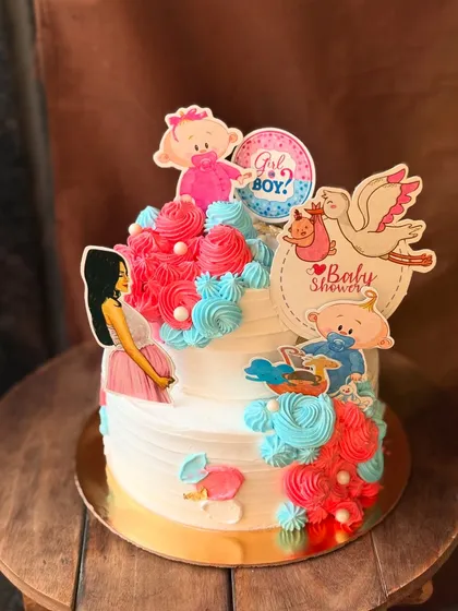 A sweet two-tier baby shower cake with pink and blue swirls, decorated with adorable toppers.