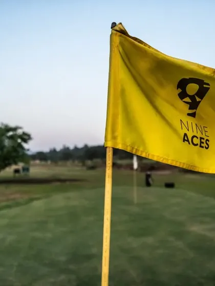 Our signature '9 Aces' flag marks the hole on a green. This close-up shot against the backdrop of the course signifies the goal for every golfer and our unique brand identity.