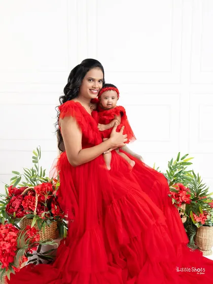 A mother and her newborn daughter in matching red outfits. This portrait captures the loving gaze of the mother and the sweet innocence of the baby.