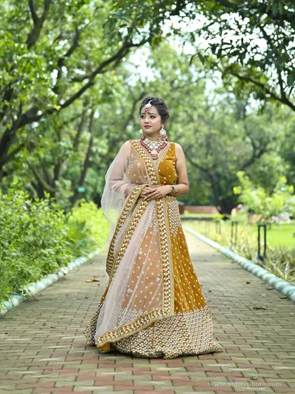 A full-length shot of the mustard yellow lehenga in a park, showcasing its vibrant color against the green background.