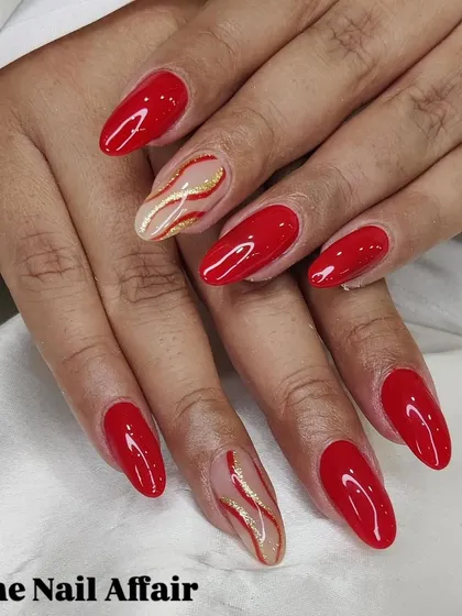 A classic red manicure with two accent nails featuring elegant gold and red glitter swirls.
