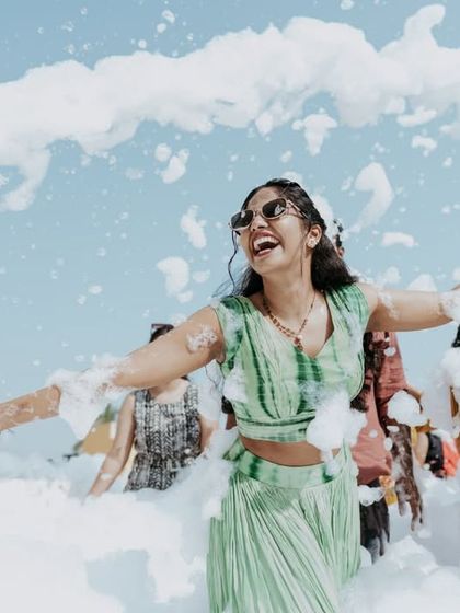A joyful bride with her arms outstretched, surrounded by foam at a fun pre-wedding party.